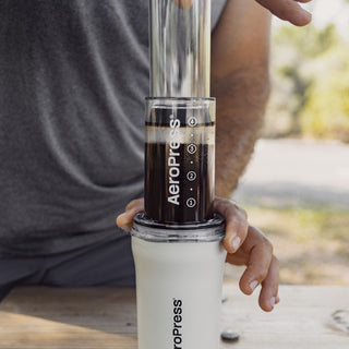AeroPress Go Plus Travel System with clear brewing chamber filled with coffee over white sturdy mug outdoors