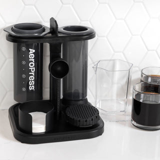 AeroPress Organizer in black plastic holding coffee filters and accessories on white countertop