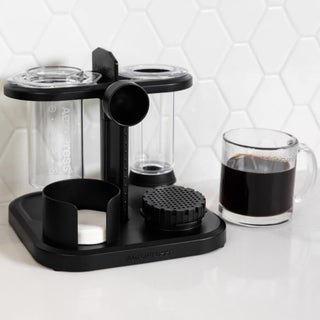 AeroPress Organizer in black sturdy plastic holding AeroPress components alongside a clear glass of coffee