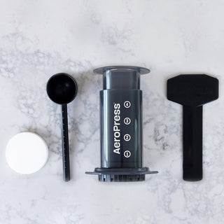 AeroPress Original Coffee Maker kit with black plunger, scoop, stirrer, and white filter cap on marble surface