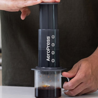 A person brewing coffee using AeroPress Original Coffee Maker black translucent plastic cylinder