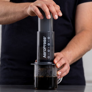 AeroPress Original Coffee Maker brewing coffee with dark liquid in clear glass cup on table