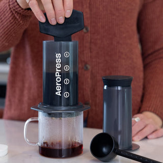 AeroPress Original Coffee Maker in use with black plastic press and clear brewing chamber above glass mug