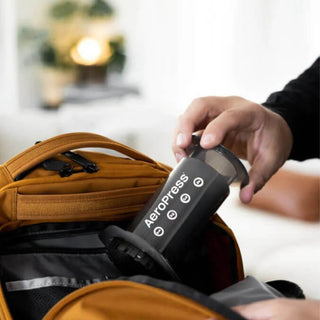AeroPress Original Coffee Maker in black being packed into a brown travel bag with zipper compartments