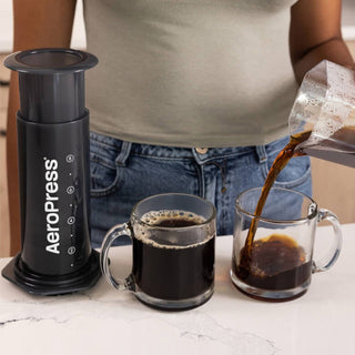 AeroPress XL Coffee Press next to two glass mugs, dark coffee being poured into one mug
