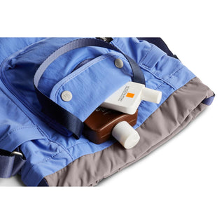 Bellroy Cinch Bucket Bag in blue with gray base showing exterior pocket holding two small bottles