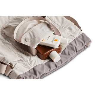Bellroy Cinch Bucket Bag in light beige with taupe base and front pocket holding skincare bottles