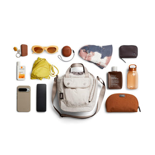 Bellroy Cinch Bucket Bag in light beige with adjustable strap shown with daily essentials flat lay