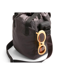 Bellroy Cinch Bucket Bag in dark recycled nylon with side pocket holding sunglasses and device