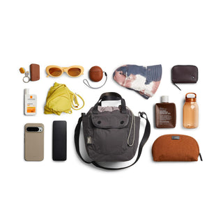 Bellroy Cinch Bucket Bag in charcoal gray nylon with adjustable strap and front pocket shown with everyday essentials