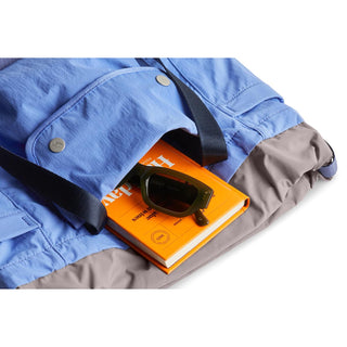Bellroy Cinch Tote in blue and grey fabric with black straps holding an orange book and sunglasses