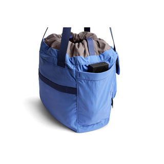 Bellroy Cinch Tote in blue recycled nylon with drawstring top and exterior pocket holding a small device