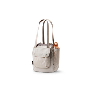 Bellroy Cinch Tote in light beige with front pocket and side bottle holder carrying copper bottle