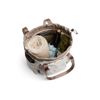 Bellroy Cinch Tote in beige with shoulder straps, showing spacious interior with organized pockets and items inside