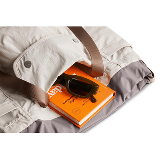 Bellroy Cinch Tote with beige recycled fabric and brown straps holding book and sunglasses