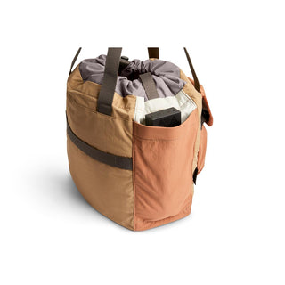Bellroy Cinch Tote in tan with drawstring closure and exterior pocket holding a small device