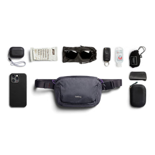 Bellroy Lite Belt Bag in dark grey recycled fabric with compact daily essentials arranged around it