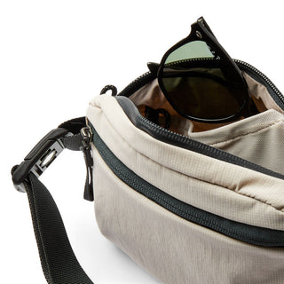 Bellroy Lite Belt Bag in beige fabric with black zipper and sunglasses inside pocket