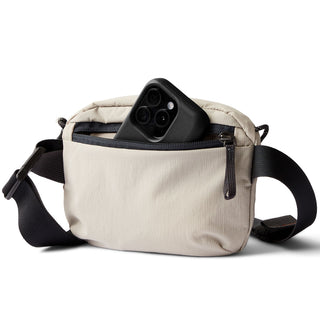 Bellroy Lite Belt Bag in beige recycled fabric with black zipper and adjustable strap holding a smartphone