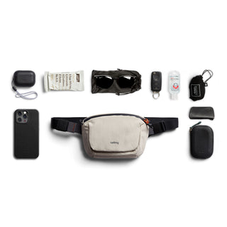 Bellroy Lite Belt Bag in beige with black strap shown with everyday essentials on white background