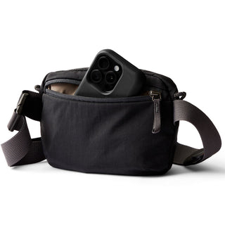 Bellroy Lite Belt Bag in black recycled nylon with front zip pocket holding smartphone