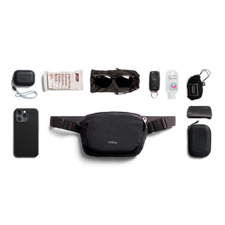 Bellroy Lite Belt Bag in black nylon with everyday essentials arranged around it on white background