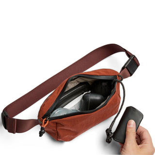 Bellroy Lite Belt Bag in burnt orange with adjustable strap and zippered main compartment open with items inside