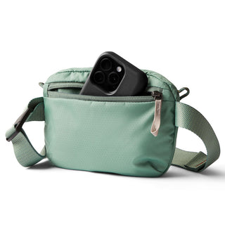 Bellroy Lite Belt Bag in green recycled fabric with front pocket holding a black smartphone