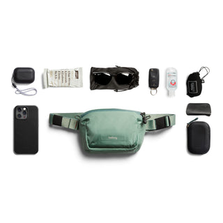 Bellroy Lite Belt Bag in green with everyday essentials arranged around it on white background