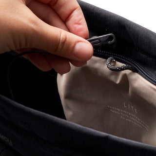 Close-up of hand opening black Bellroy Lite Totepack showing interior fabric and zipper detail