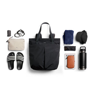 Bellroy Lite Totepack in black recycled nylon shown with travel essentials on white background