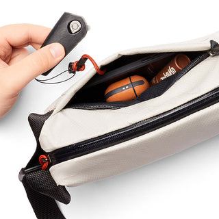 Bellroy Lite Sling Mini in light beige showing interior with tech accessories and hand holding key fob