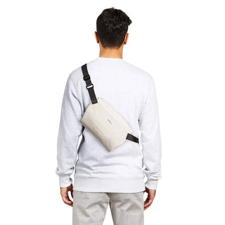 Bellroy Lite Sling Mini worn crossbody in light beige with black adjustable strap visible from back