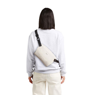 Bellroy Lite Sling Mini worn crossbody in light beige with adjustable black strap from rear view
