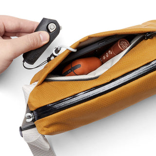 Bellroy Lite Sling Mini in caramel with an open zipper revealing contents inside the compact bag