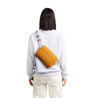Bellroy Lite Sling Mini in mustard yellow, worn crossbody with adjustable strap on back view