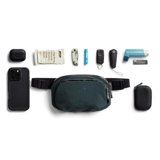 Bellroy Venture Hip Pack 1.5L in dark green with durable recycled fabric and multiple essential items displayed