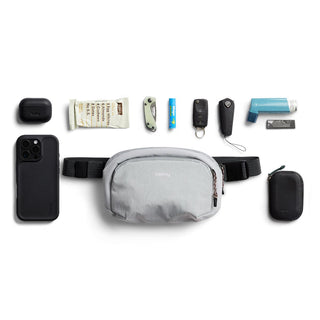 Bellroy Venture Hip Pack 1.5L in light grey fabric with everyday essentials arranged around it