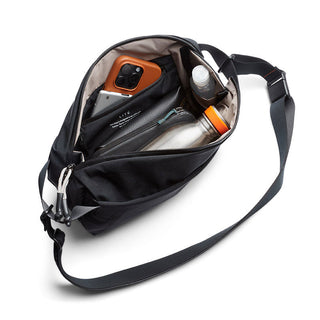Bellroy Lite Sling in black showing organized interior with phone, bottle, and accessories inside compartments