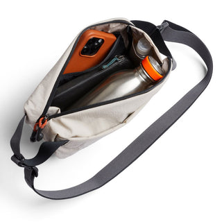 Bellroy Lite Sling Mini beige crossbody bag with adjustable strap holding bottle and phone inside