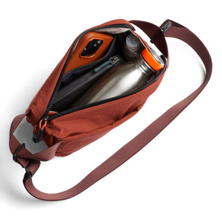 Bellroy Lite Sling Mini in rust with water bottle and small essentials inside, adjustable strap shown