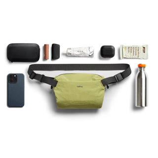 Bellroy Lite Sling Mini in olive green with adjustable black strap and everyday essentials arranged around it