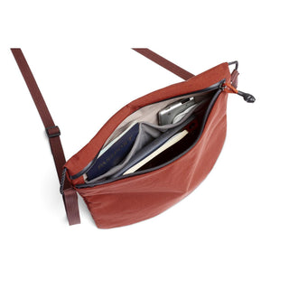 Bellroy Lite Sacoche in rust color showing organized interior compartments with passport and phone inside