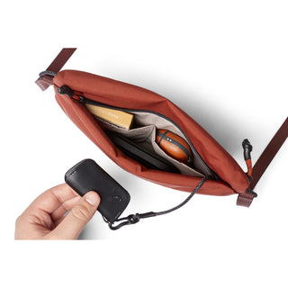 Bellroy Lite Sacoche in rust fabric with organized interior pockets and a hand holding a key fob attached inside
