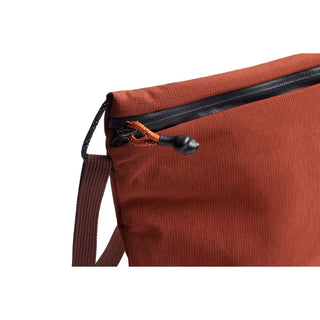 Bellroy Lite Sacoche in rust fabric with black zipper and orange pull cord detail close-up view