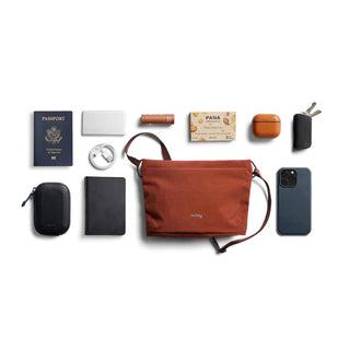 Bellroy Lite Sacoche in rust with travel essentials arranged on white background