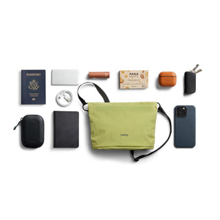 Bellroy Lite Sacoche in green with black strap surrounded by travel essentials on white background