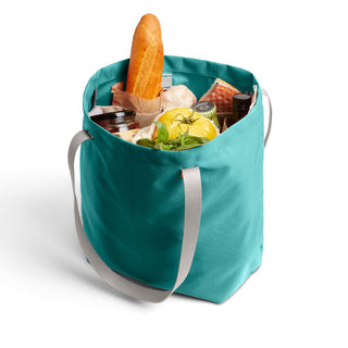 Bellroy Market Tote in teal with sturdy handles holding fresh groceries including bread and vegetables