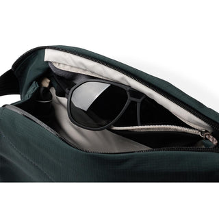 Bellroy Venture Sling 6L in dark green recycled nylon holding black sunglasses inside zippered compartment
