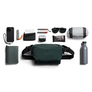 Bellroy Venture Sling 6L in dark green recycled nylon surrounded by travel essentials and accessories